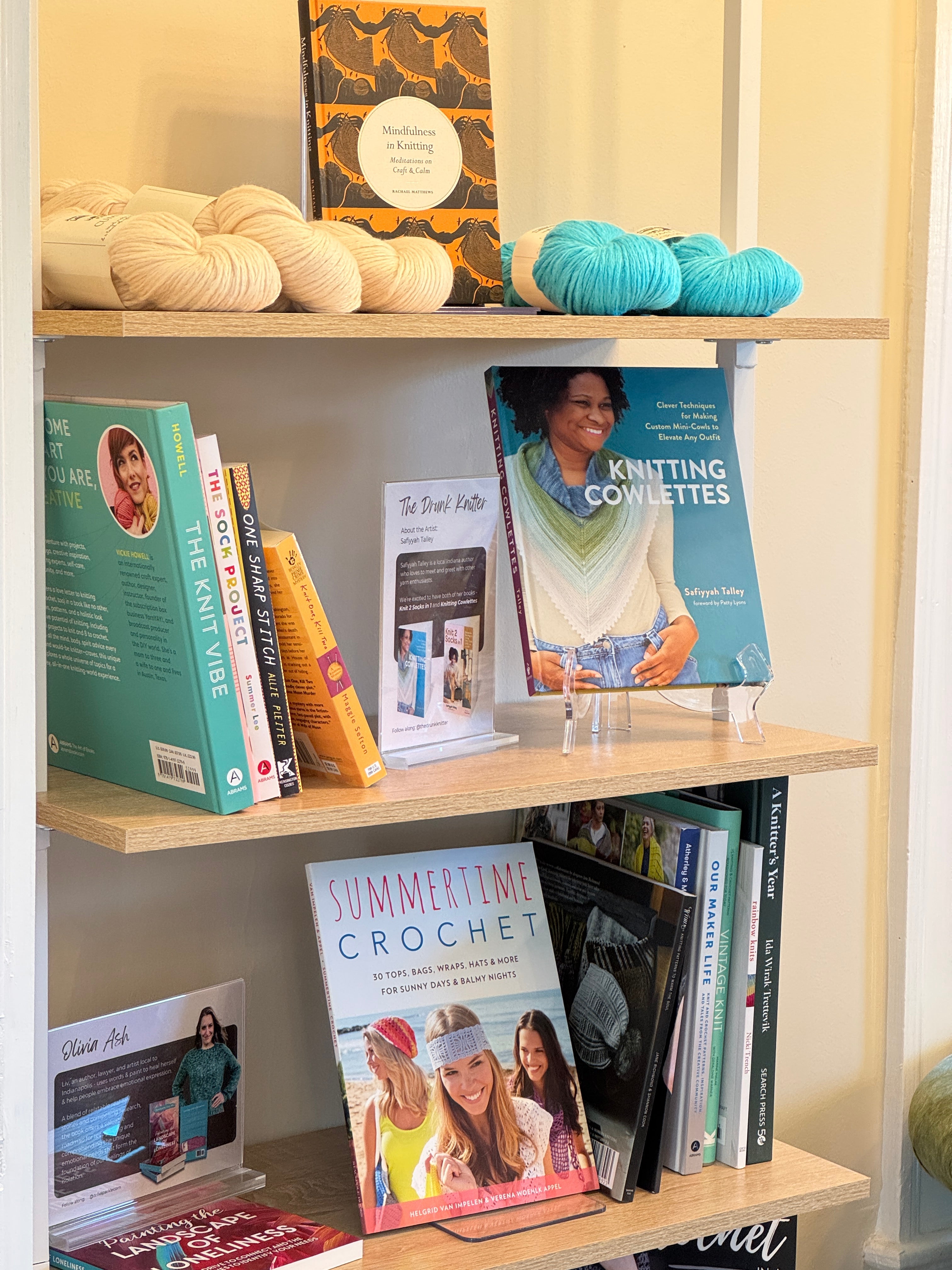 A curated bookcase featuring knitting and crochet pattern books as well as blue and white skeins of yarn