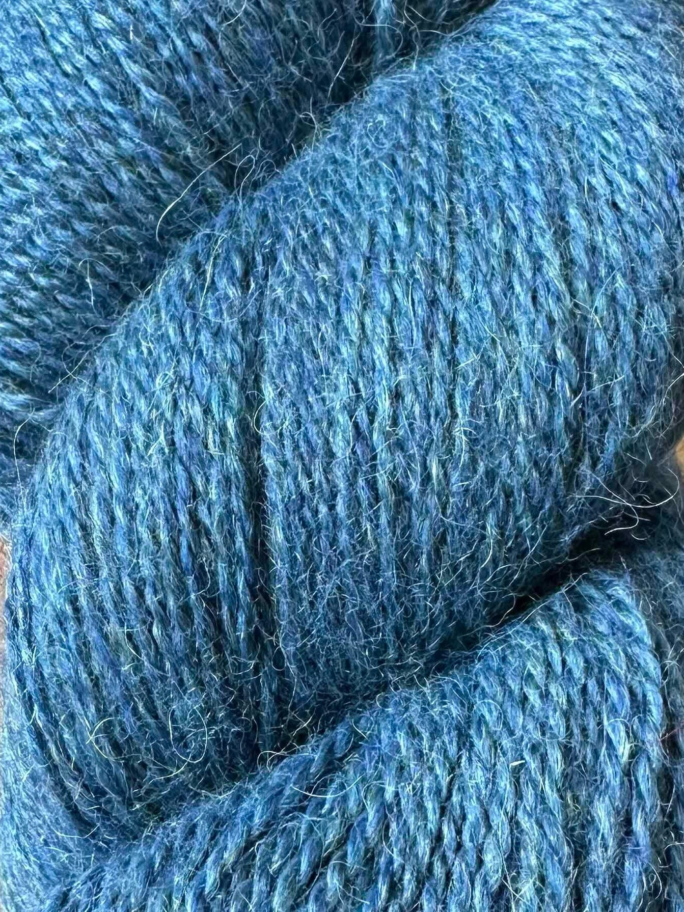 A skein of medium blue yarn with subtle heathered texture, photographed on a brown wooden surface.