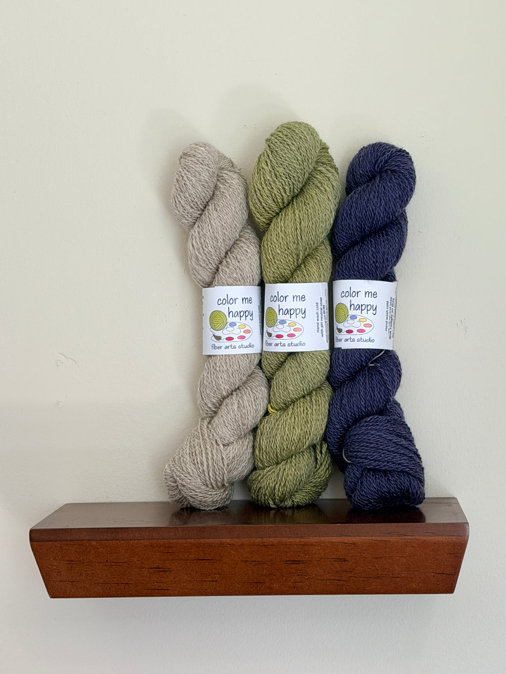 Lifestyle picture of 3 skeins of colorful yarns on a shelf.