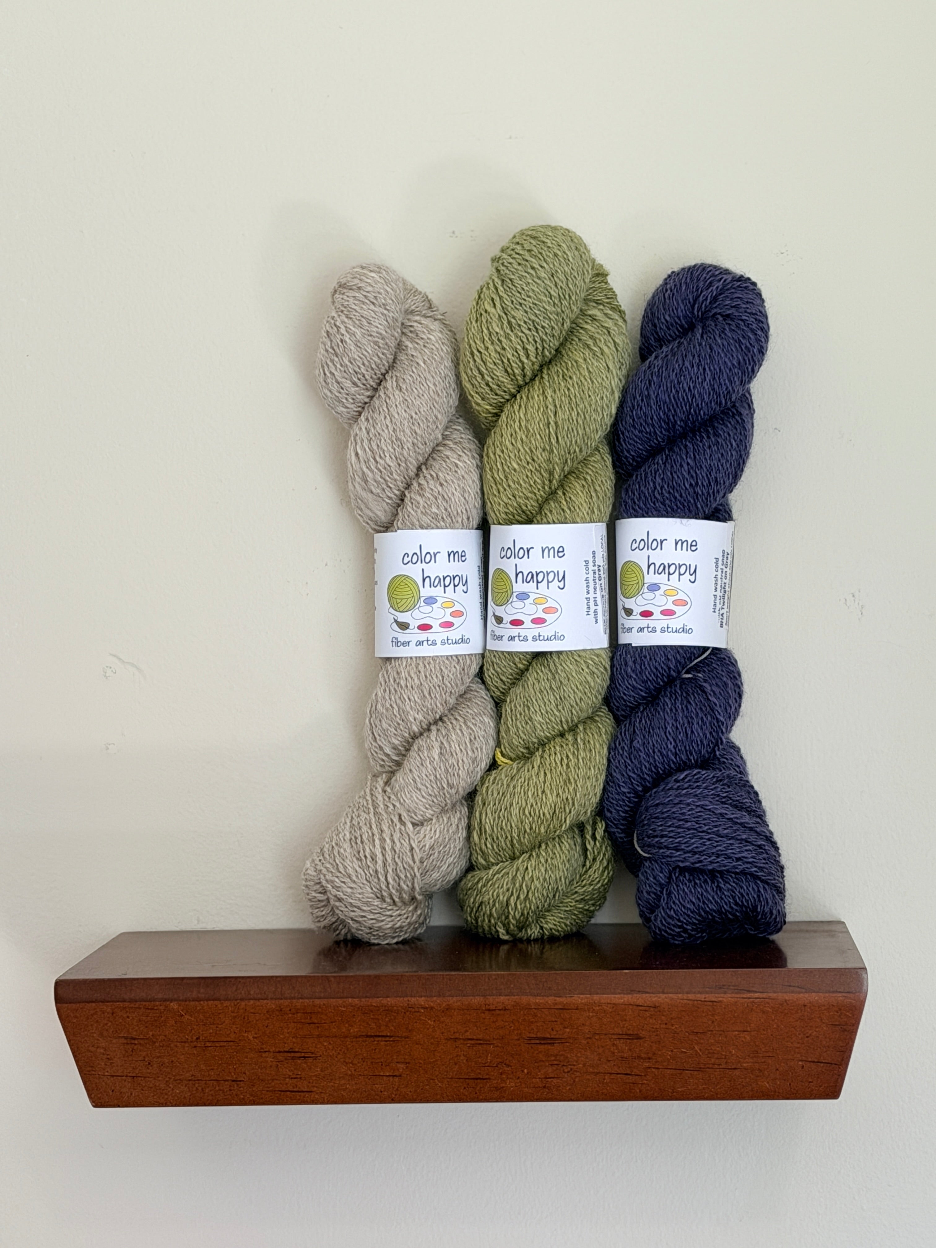 Lifestyle picture of 3 skeins of colorful yarns on a shelf.