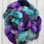 Braid of purple and teal Targhee fiber on a wooden surface