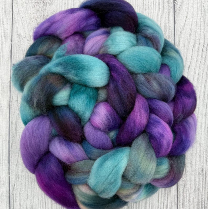 Braid of purple and teal Targhee fiber on a wooden surface