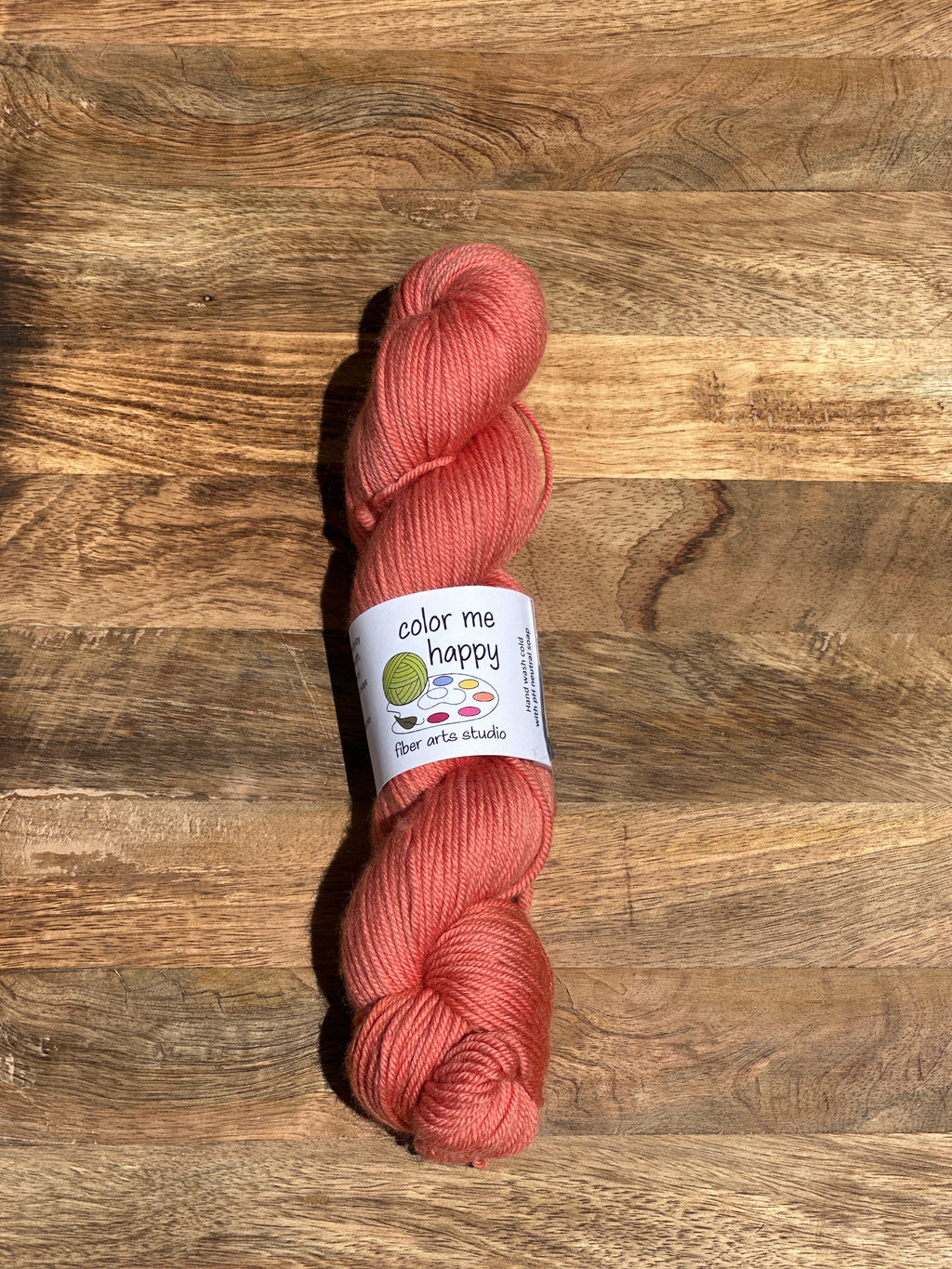 melon-colored skein of yarn with a label on a wooden surface