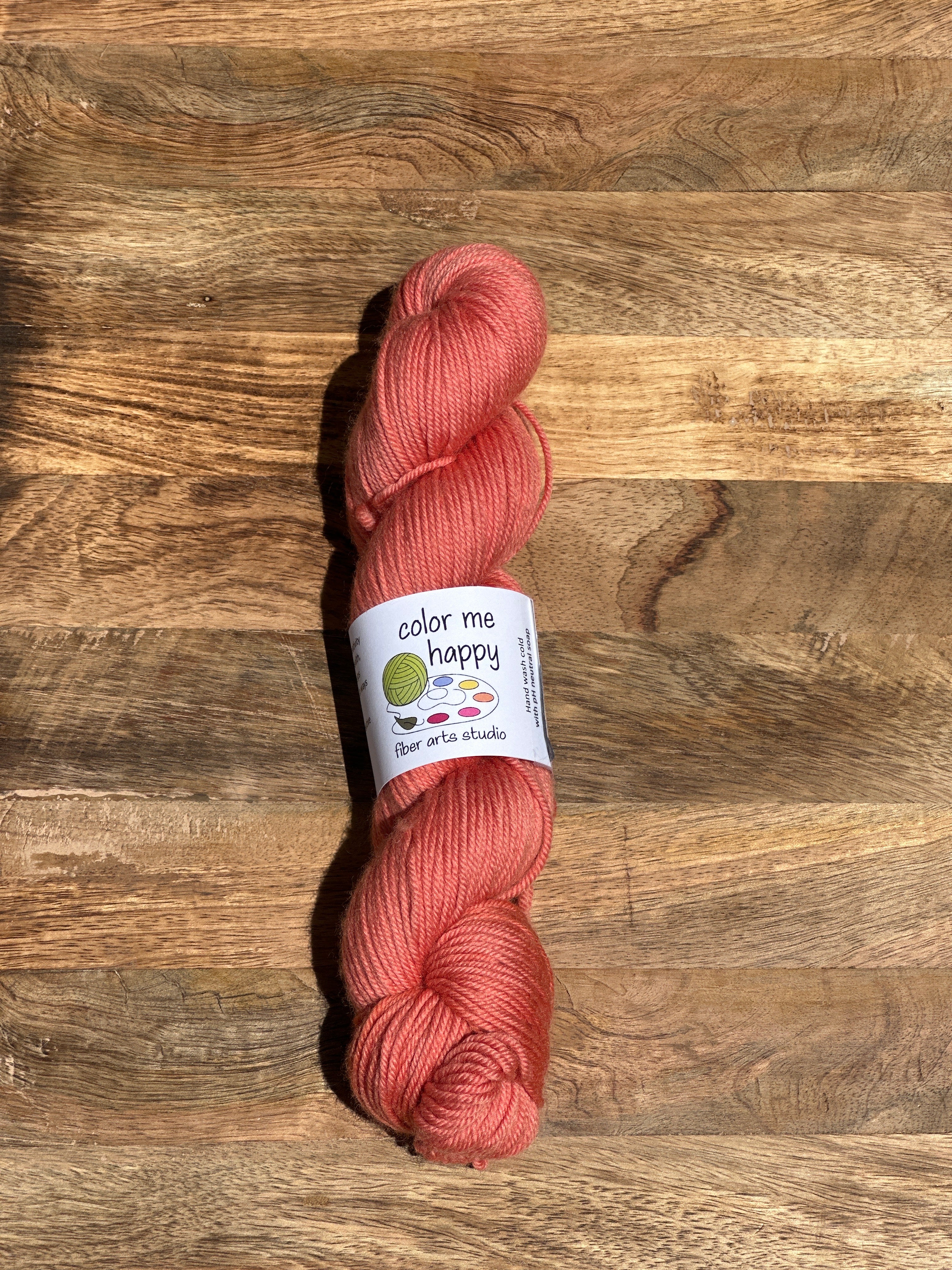melon-colored skein of yarn with a label on a wooden surface